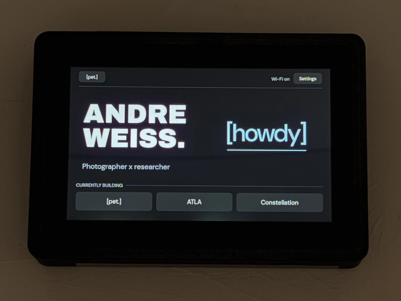 The real black PET enclosure on a wooden table, with the working home screen.