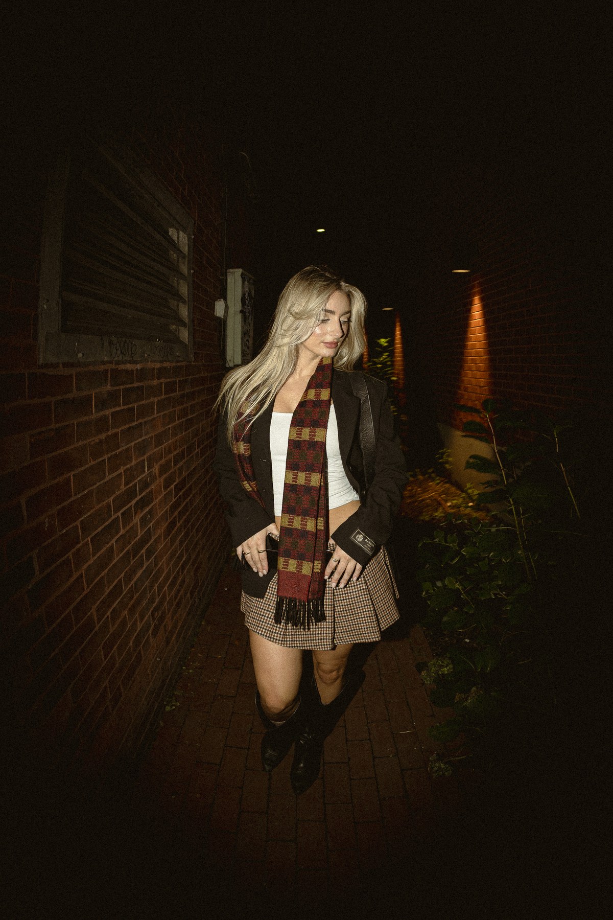 Portrait in a dark brick passage, with a red scarf and warm light.